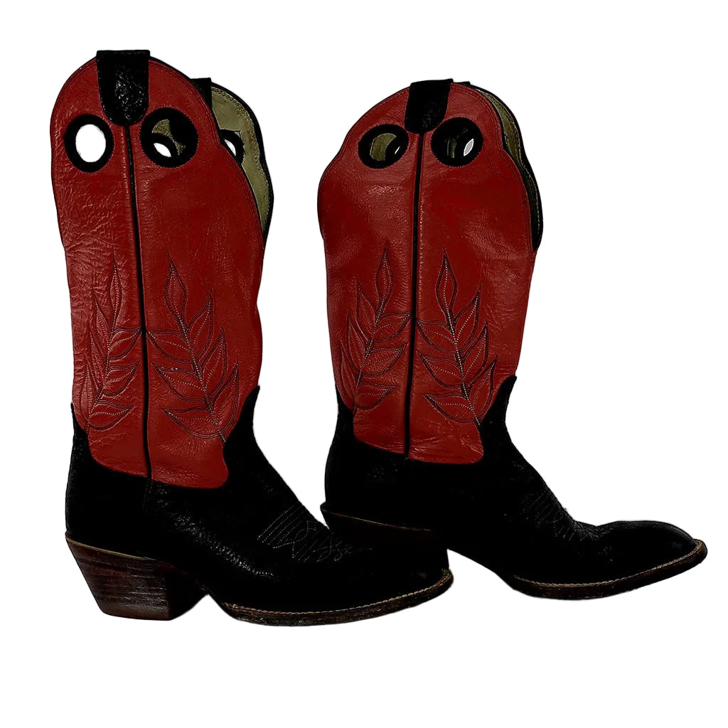 A pair of cowboy boots with a split red and black leather design, featuring cutout details on the shafts and embroidered leaf patterns.