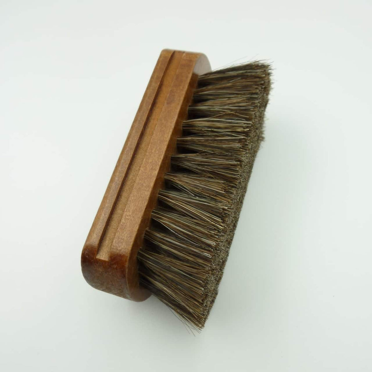 A rectangular shoe care brush with a medium brown wooden handle and dark brown horsehair bristles, photographed on a plain white background.