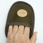 A close-up of a hand pressing down on a mesh-covered mitt with a dark brown fabric border and a circular tan Boot Collector logo patch.