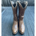 A pair of brown leather cowboy boots with a textured alligator or crocodile skin pattern, standing upright on a dark gray wooden surface.