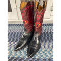 A pair of cowboy boots with black leather lower shafts and red leather upper shafts decorated with geometric and floral embroidery, standing on a blue and white patterned rug.