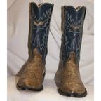 A pair of cowboy boots with dark navy blue shafts featuring gold western embroidery and a brown snakeskin-patterned foot, set against a draped white fabric background.