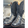 A pair of black western cowboy boots with textured alligator or crocodile skin on the lower shafts and decorative contrast stitching, displayed on a black box in a home setting.