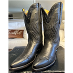 A pair of black western cowboy boots with embossed alligator-style texture and floral stitching, displayed on a dark wooden surface in a home setting.